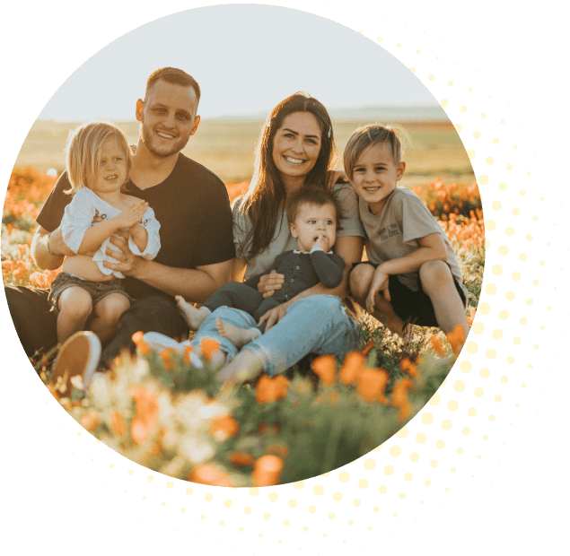 A family sitting in a field of flowers, smiling and posing for the camera.